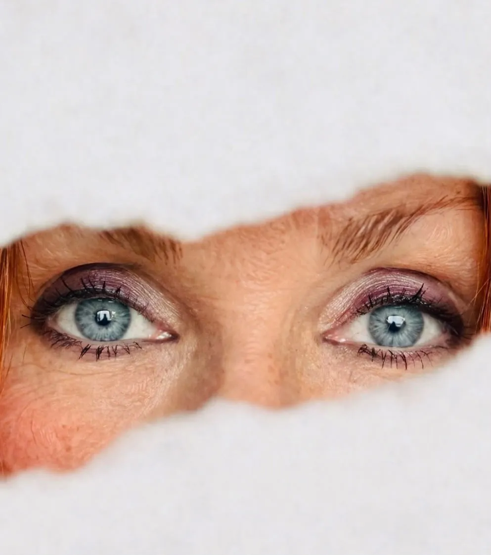 Close up of Cate McMurray's blue eyes through torn paper
